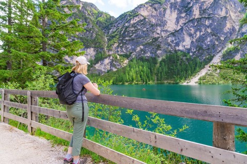 Person looking from a wooden fence at a mountain lake, surrounded by nature, Lake Braies, South