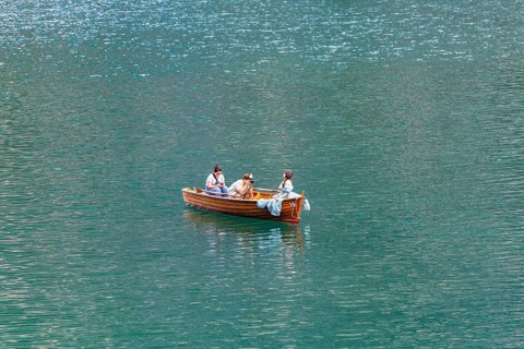Three people in a small wooden boat on a quiet lake enjoying a relaxing trip, Lake Braies, South