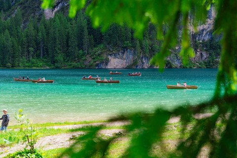 Several boats on a turquoise-coloured lake, surrounded by a green forest and summer atmosphere,