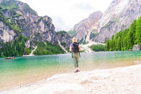 A woman enjoys the view from a lake shore of the majestic mountains all around, Pragser Wildsee,