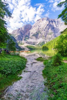A clear mountain lake surrounded by impressive mountains and dense forest under a partly cloudy