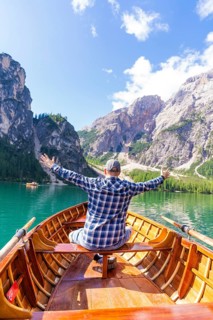 Man spreads his arms with joy on a boat on a mountain lake, Pragser Wildsee, South Tyrol,