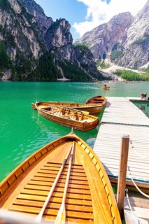 Several wooden boats are moored to a jetty on a calm, emerald-green mountain lake, Lake Braies,
