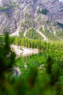 A mountainous background behind a green forest reflected in a clear lake, Pragser Wildsee, South