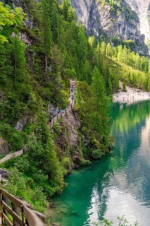 A narrow path winds along a steep slope with a view of an emerald green lake, Pragser Wildsee,