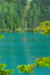 A small red boat on a turquoise-blue lake, surrounded by dense forest, Pragser Wildsee, South