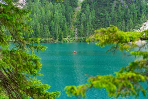 A single boat on a calm turquoise-blue lake, framed by green trees, Pragser Wildsee, South Tyrol,