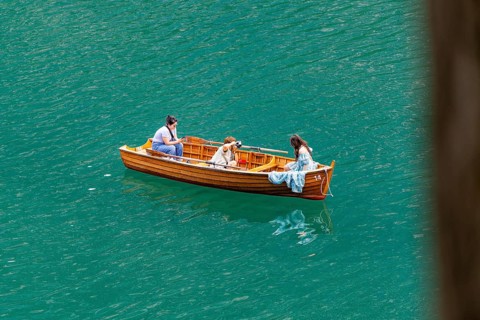 Three people in a wooden boat, floating relaxed on the water, in peaceful surroundings, Lake