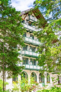 A white hotel building with balconies surrounded by green trees, Lake Braies, South Tyrol,