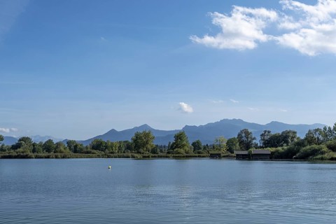 Tranquil lake with views of wooded shores and mountain landscape under a clear blue sky, Chiemsee,