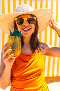 Happy woman wearing a straw hat and sunglasses holding a pineapple shaped cocktail in front of