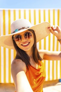 Fashionable tourist enjoying a sunny beach day, capturing joyful moments with a selfie while