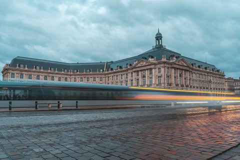 Long exposure photo of a tram passing by the stock exchange palace of bordeaux, france, in a cloudy