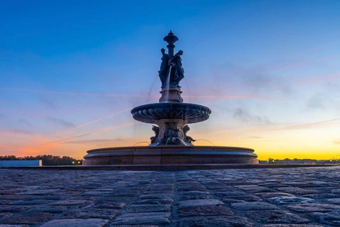 The three graces fountain in bordeaux, france, stands majestically against a vibrant sunrise sky,