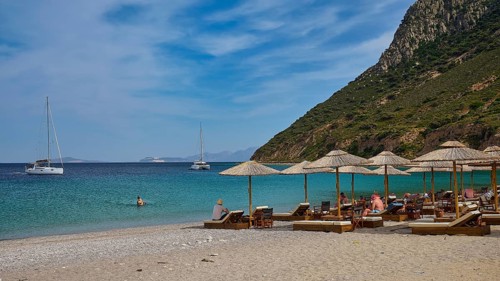 Kamari beach, summer beach scenery with deckchairs and parasols, two sailing boats in the calm blue