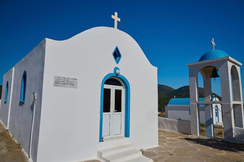 Chapel of Agios Charalambos, White chapel with blue detail and a bell tower under a clear sky,
