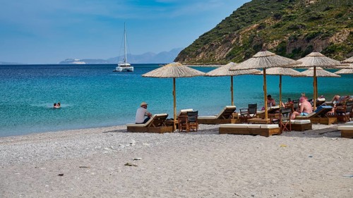 Kamari beach, Relaxed beach with sun loungers and parasols, Sailboat on the horizon in clear blue