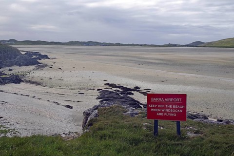 Empty beach with a warning sign in the foreground, surrounded by dunes and a wide sky, airport,