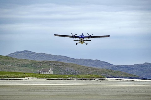 Low flying aeroplane over a runway in mountain landscape with cloudy sky, Isle of Barra, Hebrides,