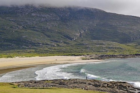 Expansive coastline with beach and waves against a mountain backdrop under a cloudy sky, Castlebay,