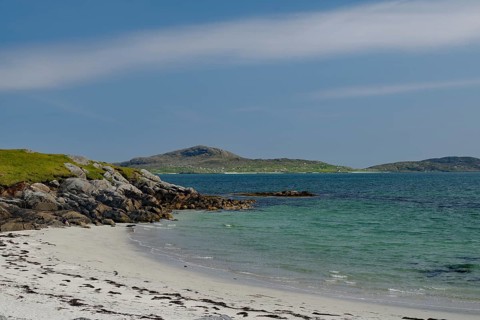 Quiet beach with white sand and rocks, surrounded by blue sea and clear sky, Eriksay, South Uist,