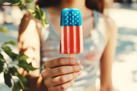 Woman holding melting American flag colored popsicle on sunny beach symbolizing summer and