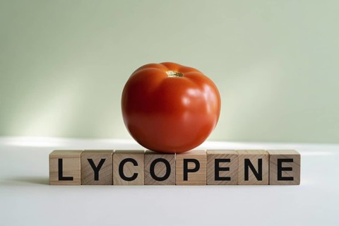 Red tomato with wooden blocks spelling Lycopene. Minimalist studio image emphasizing