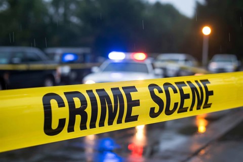 Close up of yellow crime scene tape with water droplets stretches across a rainy street with police