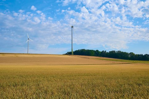Wide fields with wind turbines under a blue sky and clouds, sustainable energy source, summer,