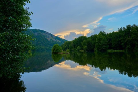 The calm river Main reflects trees and an impressive sky streaked with evening clouds, summer,