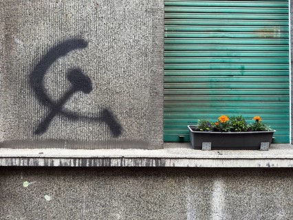 A hammer and sickle graffiti on a house wall next to a planted flower box in front of a roller