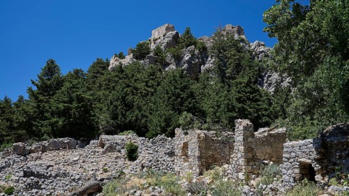 Ancient ruins in front of a wooded hill with clear blue sky in the background, Abandoned Village,