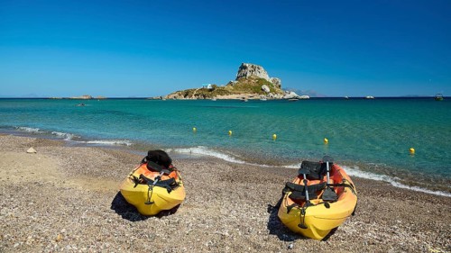 Two kayaks on the beach with a view of a small island in the blue sea, Agios Stefanos Beach, Agios