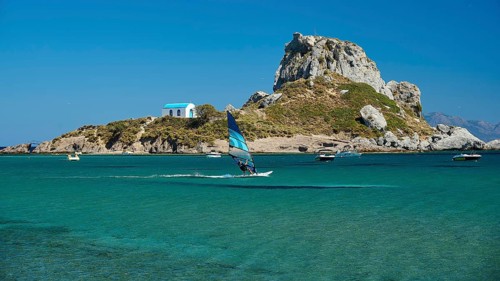 View of island with windsurfer and chapel in bright sunshine, Agios Stefanos Beach, Agios Stefanos