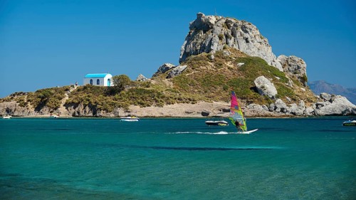 Island with windsurfer and chapel, surrounded by turquoise water, Agios Stefanos Beach, Agios