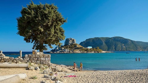 Family on the beach overlooking a green island and clear blue waters, Agios Stefanos Beach, Agios