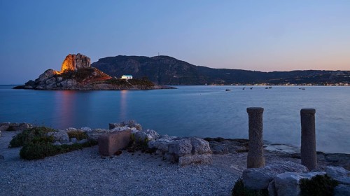 Night view of an island with illuminated rock and a small chapel in the calm water, Agios Stefanos