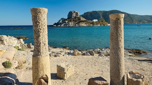 Ancient columns on the coast with a view of an island and the blue sea, Agios Stefanos Beach, Agios