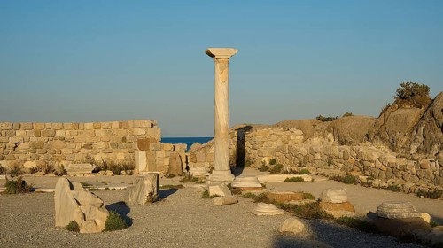 Historic site with a single preserved column surrounded by ancient walls and sea views, Agios