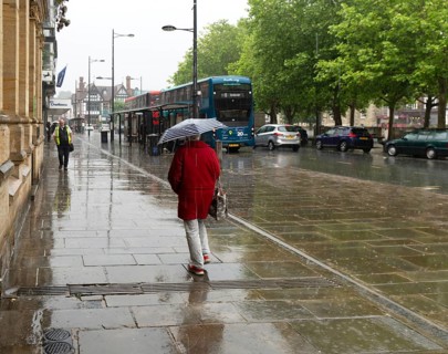 Woman with umbrella walking in heavy rain, city centre of Salisbury, Wiltshire, England, UK