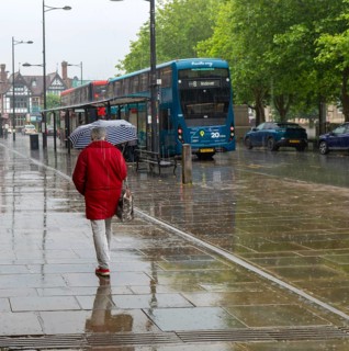 Woman with umbrella walking in heavy rain, city centre of Salisbury, Wiltshire, England, UK