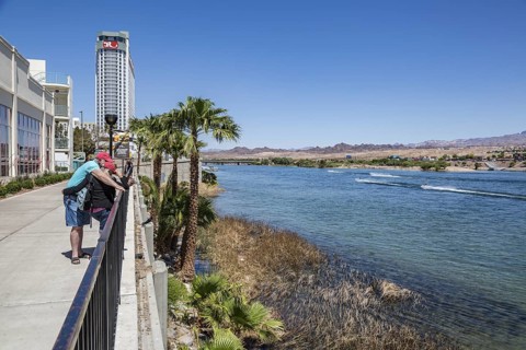 Couple looking at cell phone on sidewalk overlooking jet ski activity on the Colorado River in