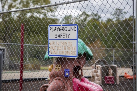 Sign with playground safety rules on a chain link fence surrounding a childrens palyground