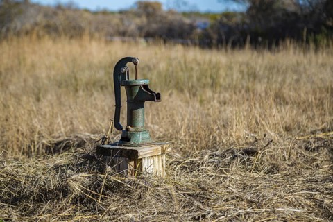 Old fashioned manual hand pump on water well in grassy field