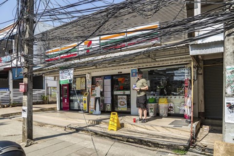 American tourist standingunder a tangled mess of utility wires outside a 7 Eleven store in Chiang
