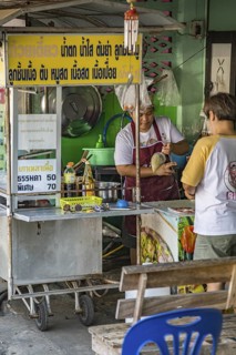 Man purchasing food from a sidewalk food cart in Chiang Rai province of Northern Thailand