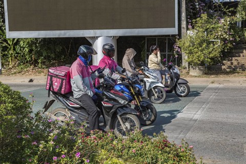 Food delivery drivers and other Thai motor scooter riders at a traffic light in Chiang Rai,