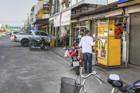 Thai man filling motor scooter with gasoline from a remote Sun Oil pump in Chiang Rai, Thailand
