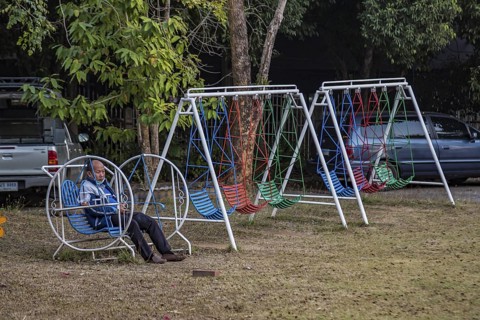 Thai man sitting alone on a childs playground swing in Chiang Rai, Thailand