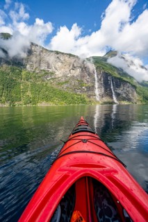 Kayak trip on the Geirangerfjord with waterfall The Seven Sisters, tip of a red kayak in the fjord,